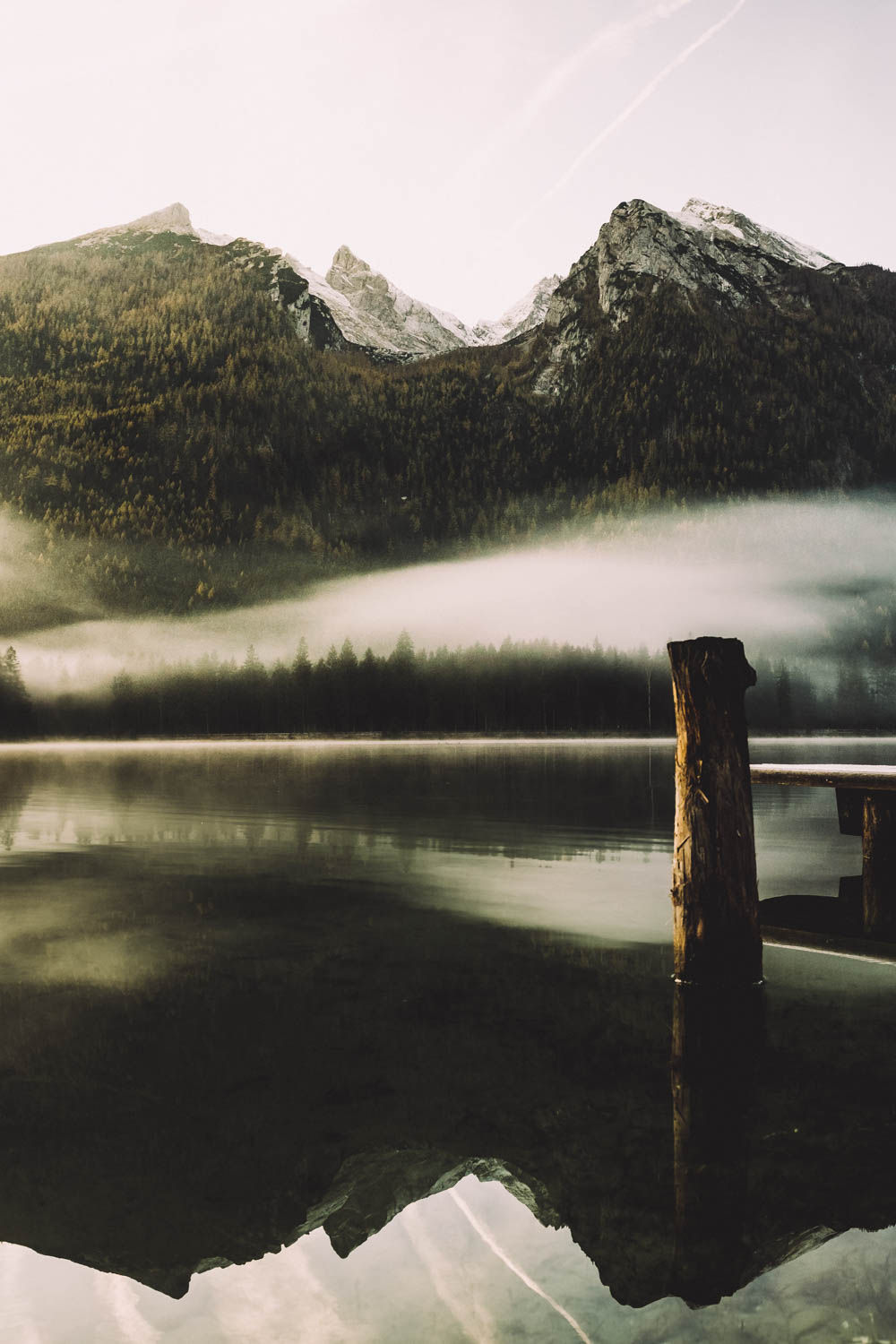 Das Gebirge spiegelt sich in der glatten Wasseroberfläche. Nur ein Holzpfahl „durchbricht“ die Ruhe.