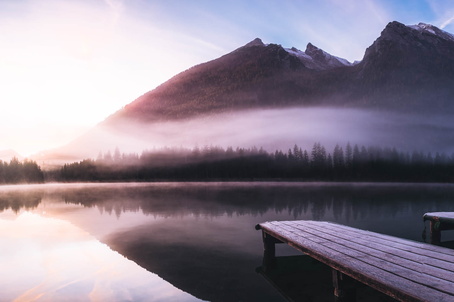 Die Bootsstege ragen in den Hintersee. Im Hintergrund ragen die Gipfel des Hochkaltermassivs in den Morgenhimmel.