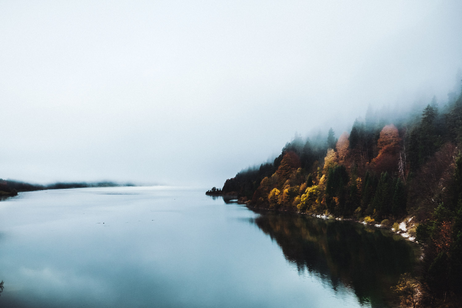 Auf der anderen Seite spiegeln sich die vom Nebel umhüllten Bäume im ruhigen Wasser des Sees.