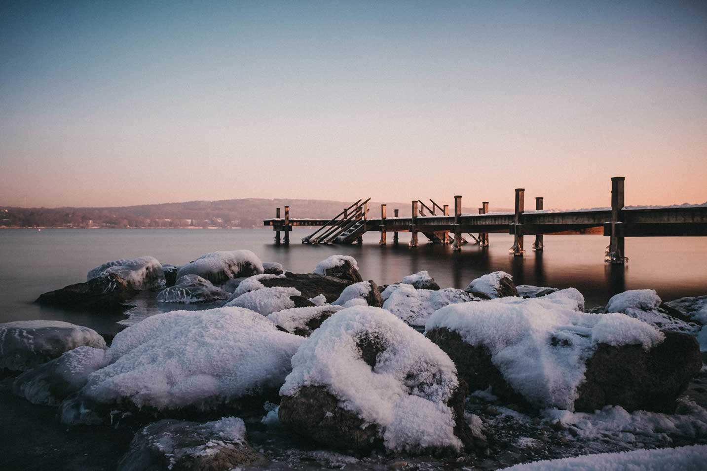Das mit Schnee bedeckte Ufer und ein Steg ragen in den Starnberger See.
