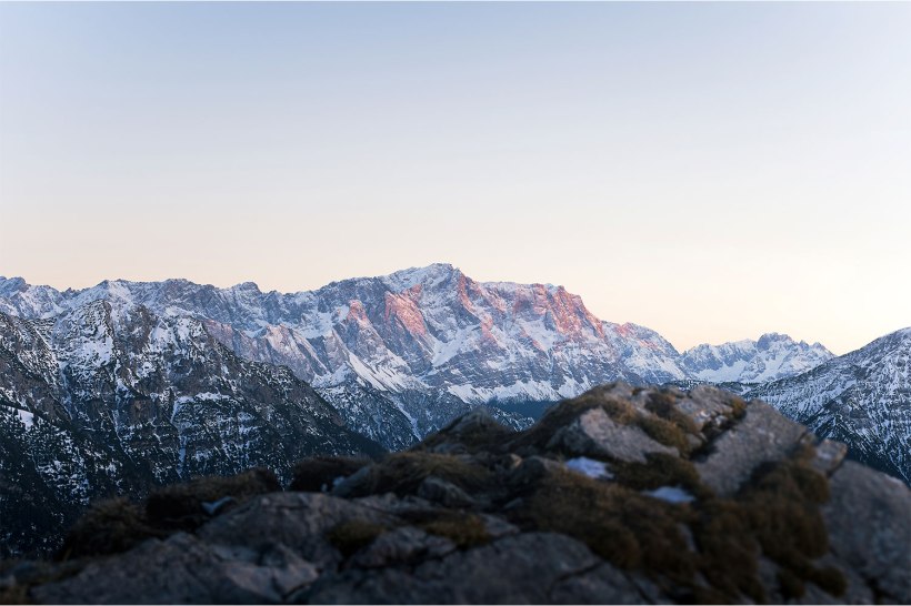 die schneebedeckte zugspitze im Abendrot mit verschwommenen steinen im vordergrund