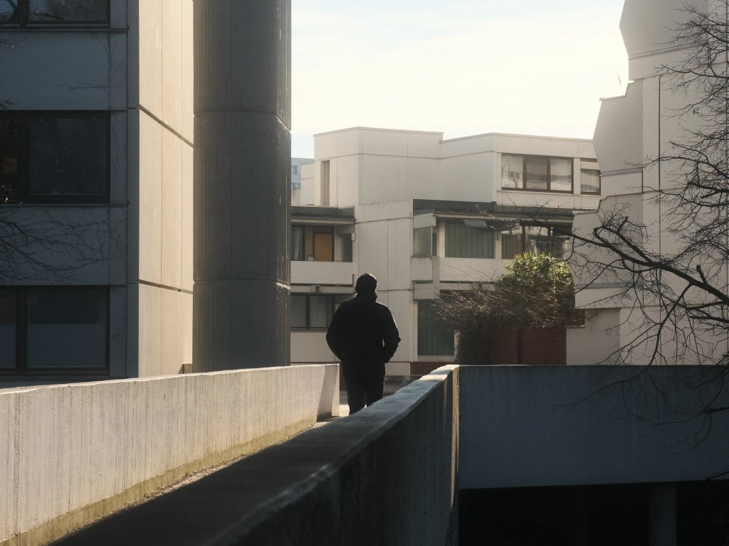 Eine Alltagsszene im Olympiadorf in München. Ein Mann geht über eine Brücke