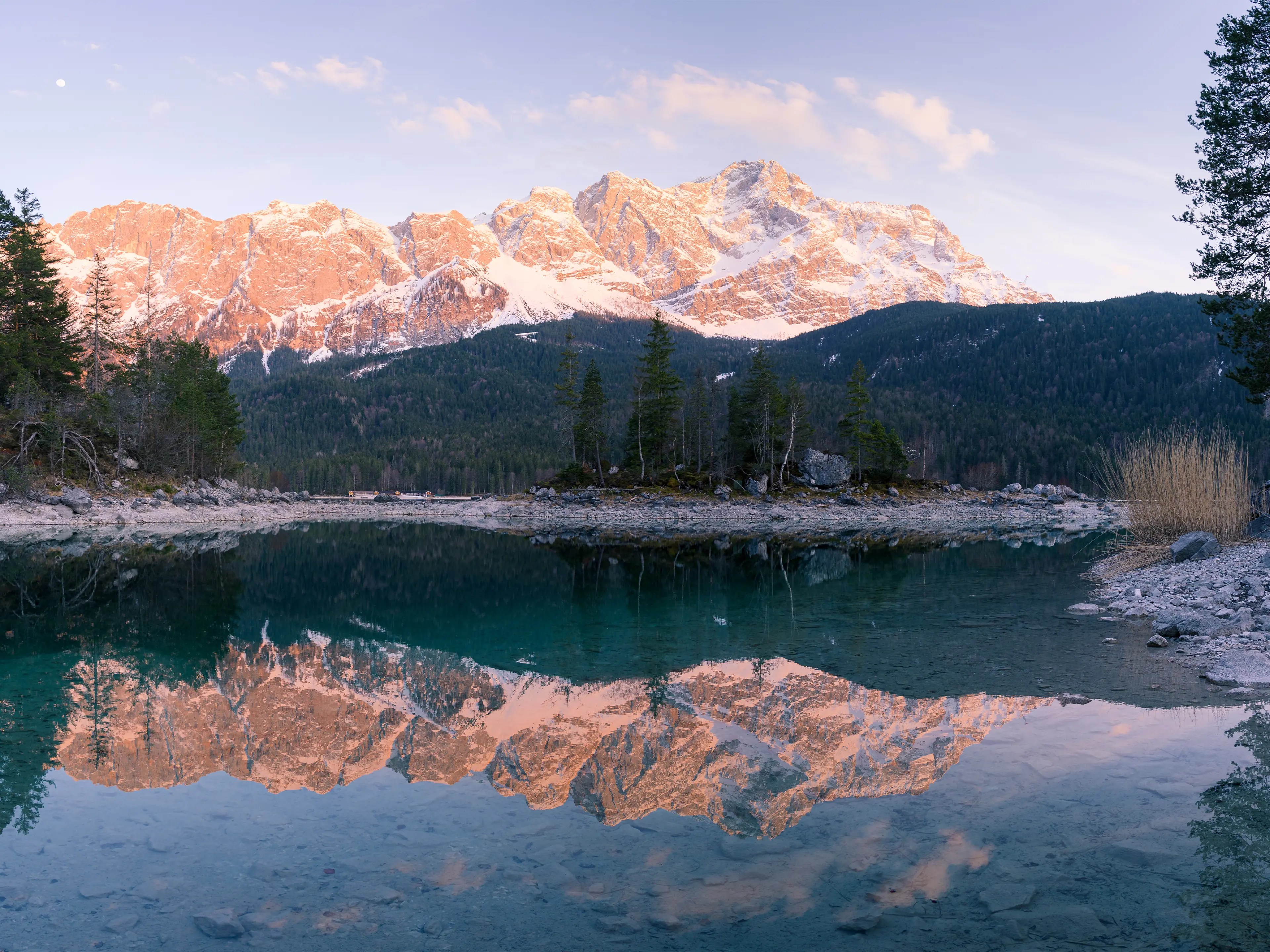 Die Zugspitze leuchtet im rot in Abendlicht und spiegelt sich im See.