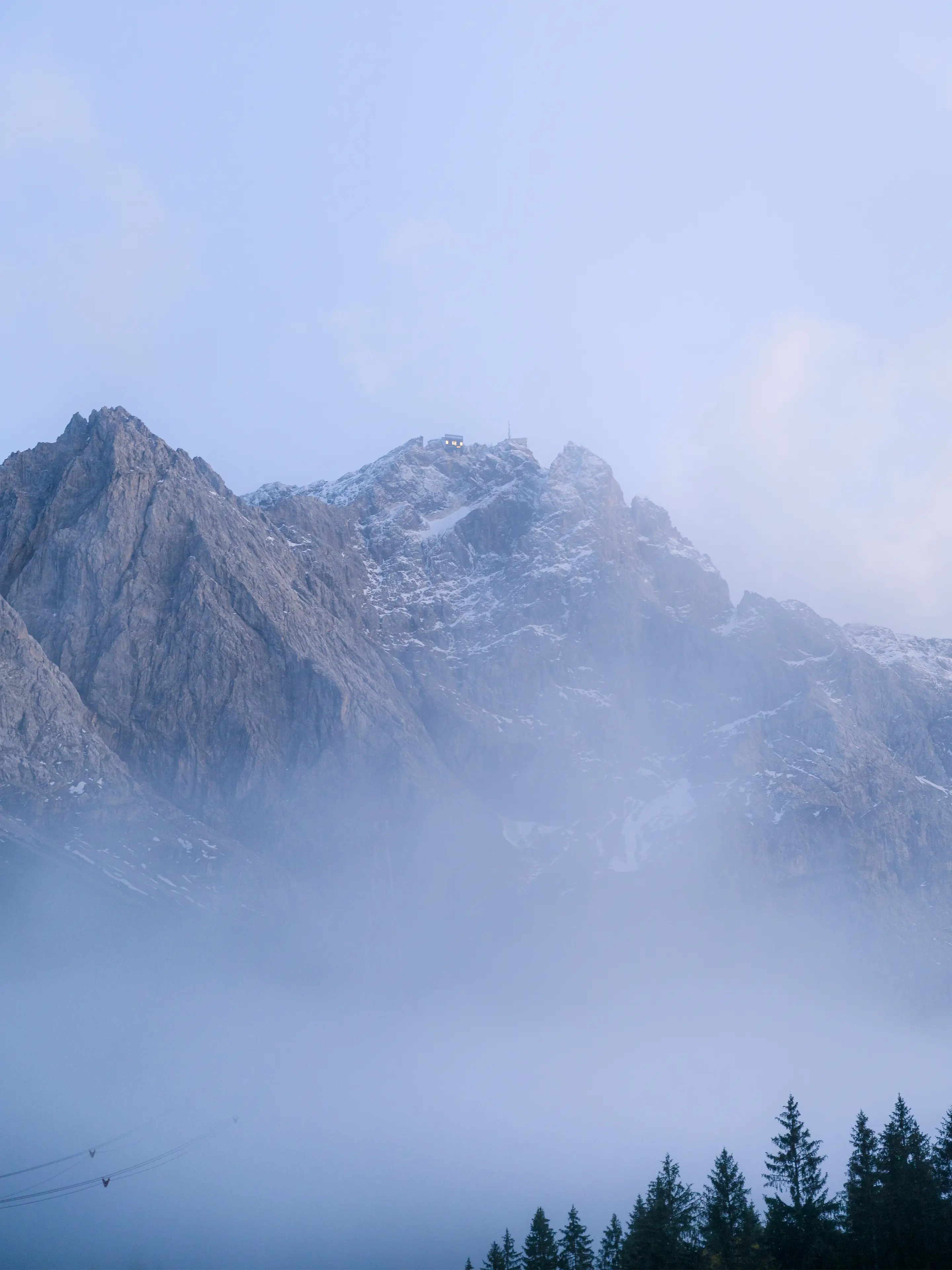Blick zur Zugspitze aus dem Tal. Im Tal liegt leichter Nebel und der Gipfel ragt aus dem Nebel heraus