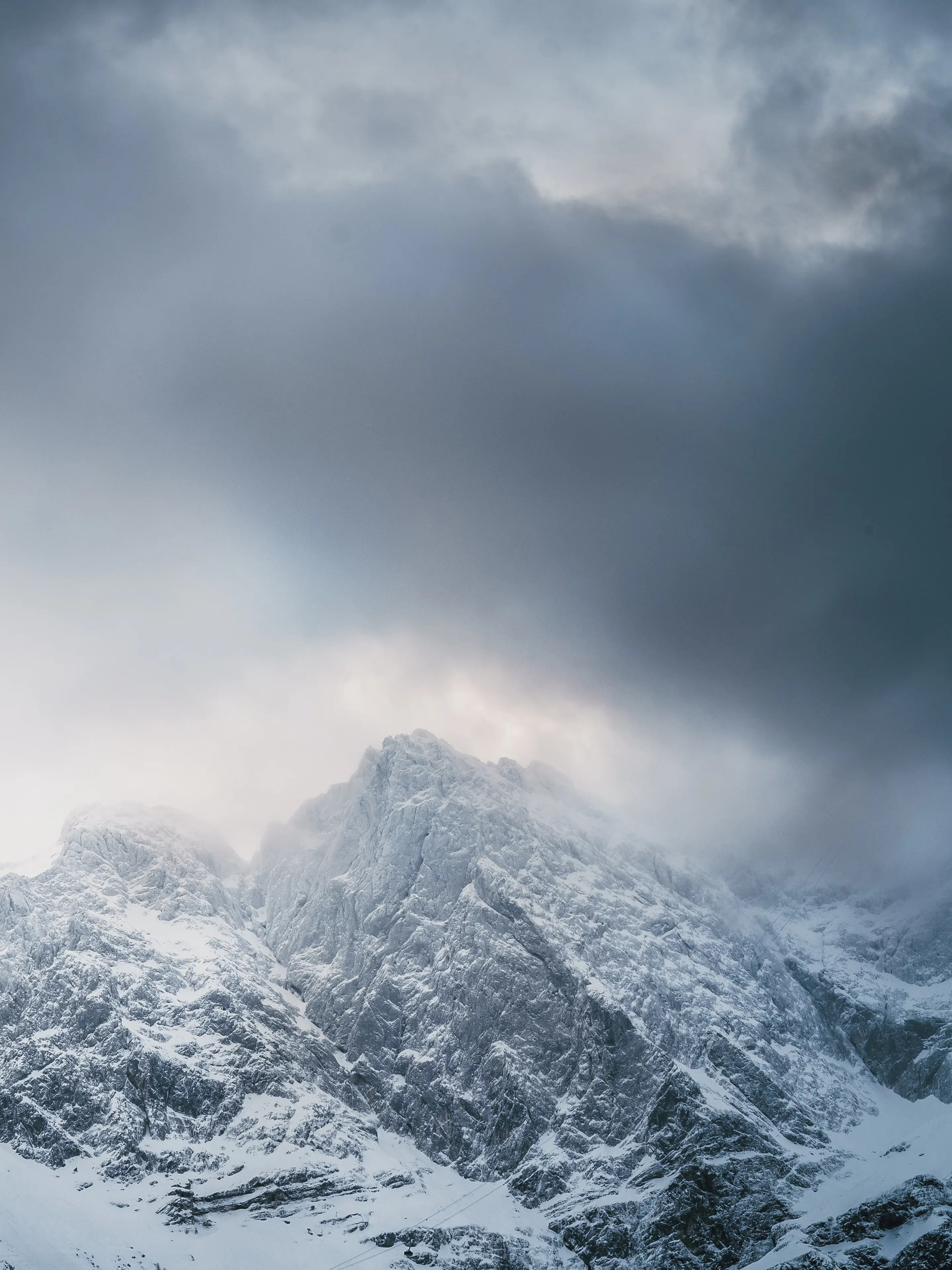 Dunkle Wolken ziehen über einen verschneiten Gipfel.