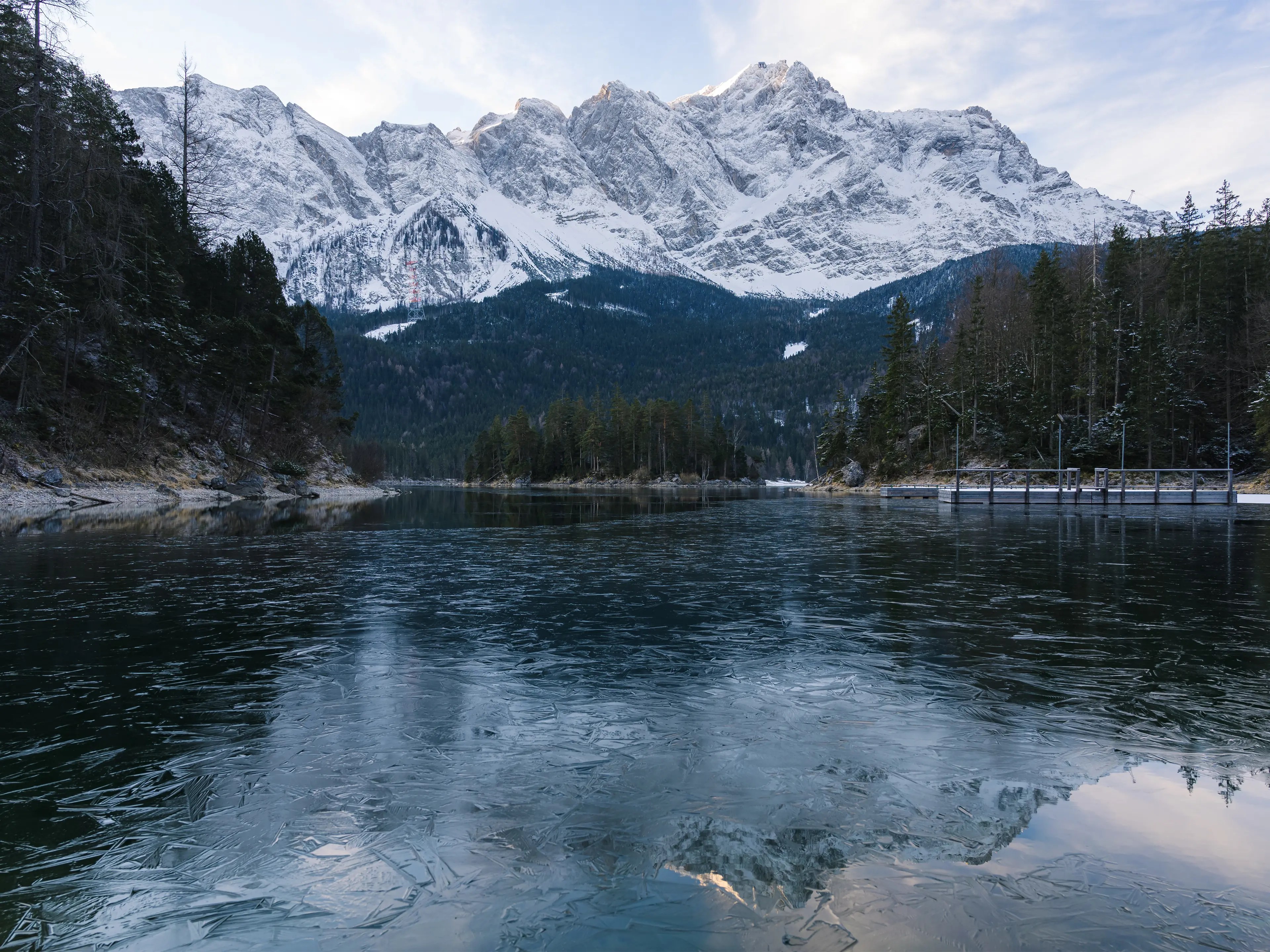 Im März ist der Eibsee meist noch teilweise zugefroren. Die schneebeckten Gipfel rund um die Zugspitze leuchten nur leicht in der Morgensonne.