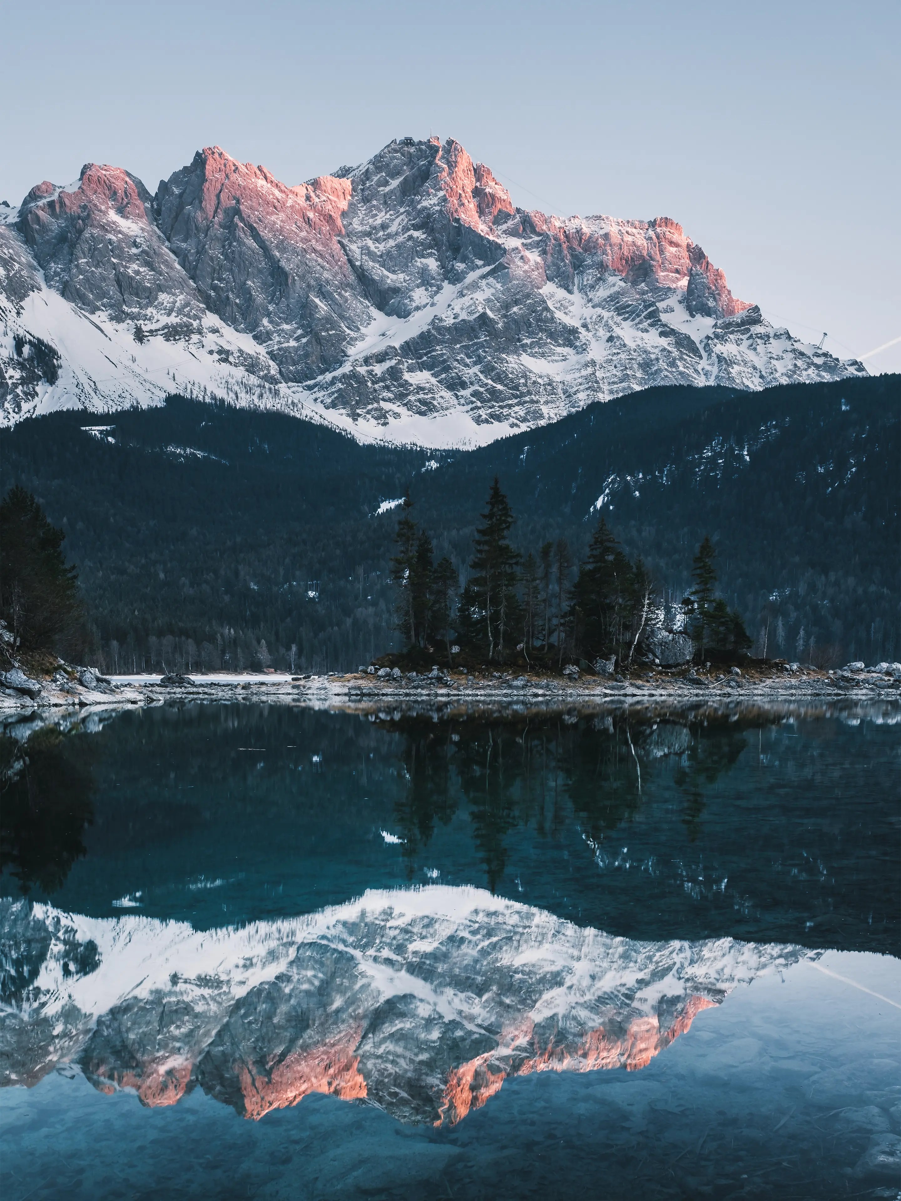 Der Gipfel der Zugspitze leuchtet im rot in Abendlicht und spiegelt sich im See.