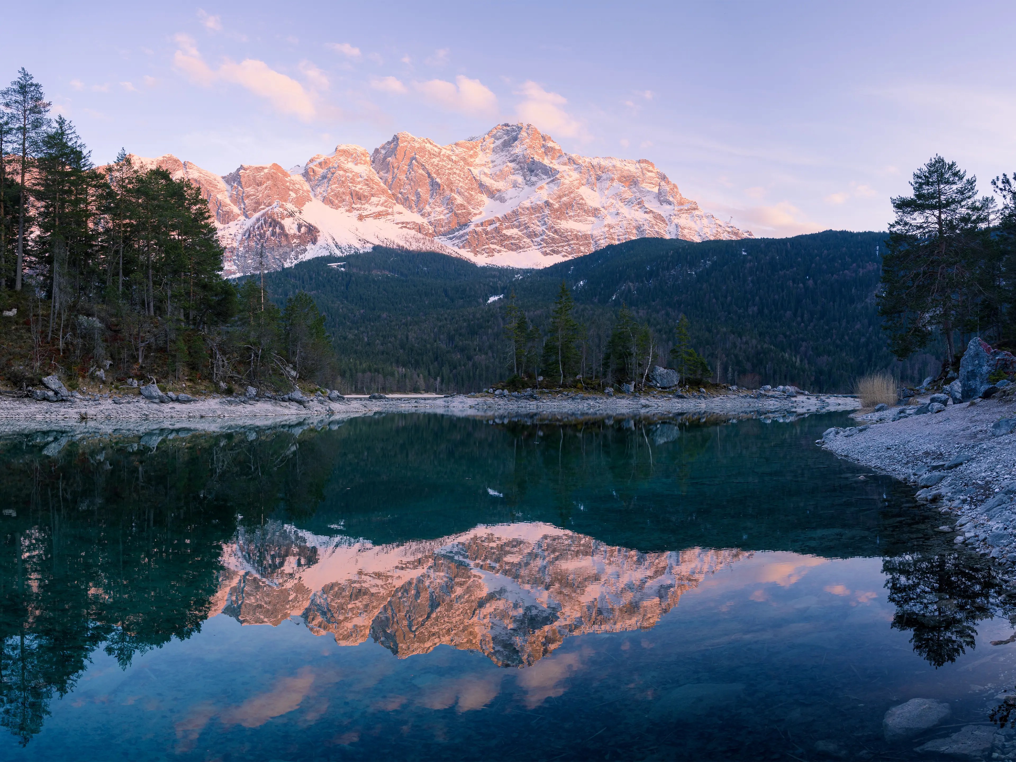 Die Zugspitze leuchtet im rot in Abendlicht und spiegelt sich im See.