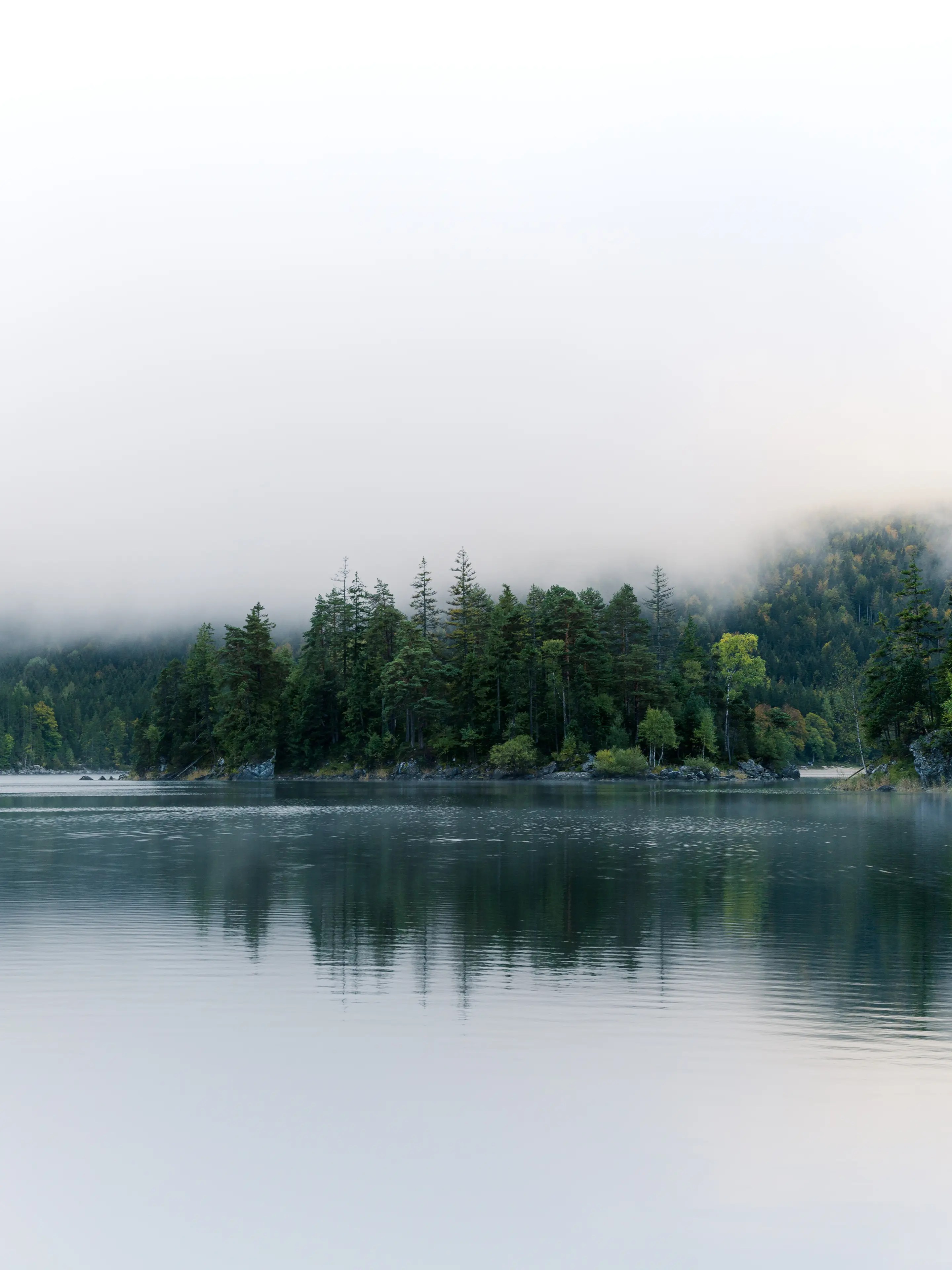 Tiefe Wolken verdecken den Blick zu den Bergen. Es ist eine Insel mit Bäumen zu sehen.