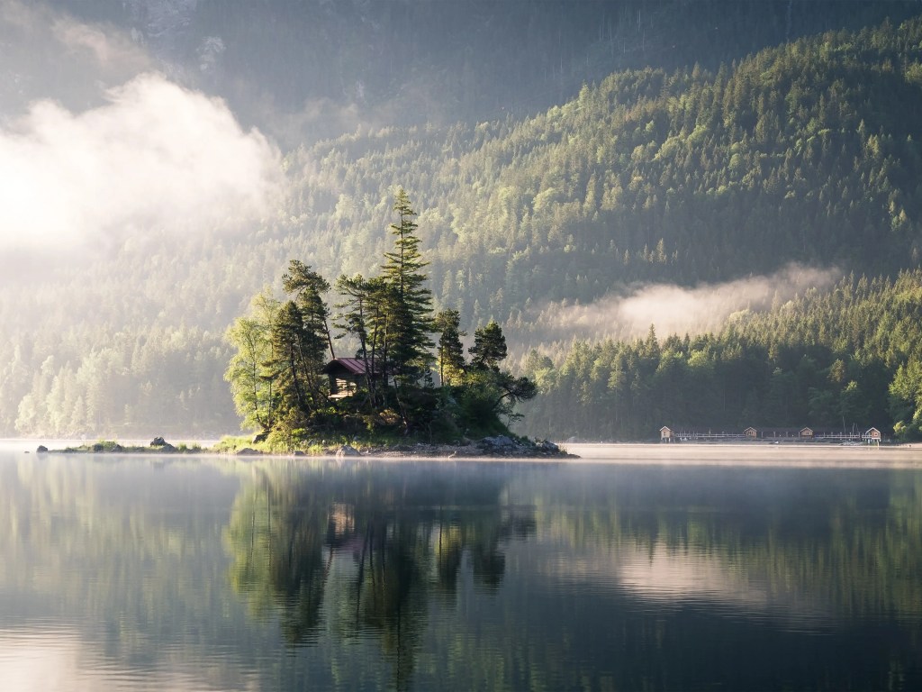 Eine kleine Insel im Eibsee, auf der Bäume und eine kleine Hütte mit rotem Dach stehen.
