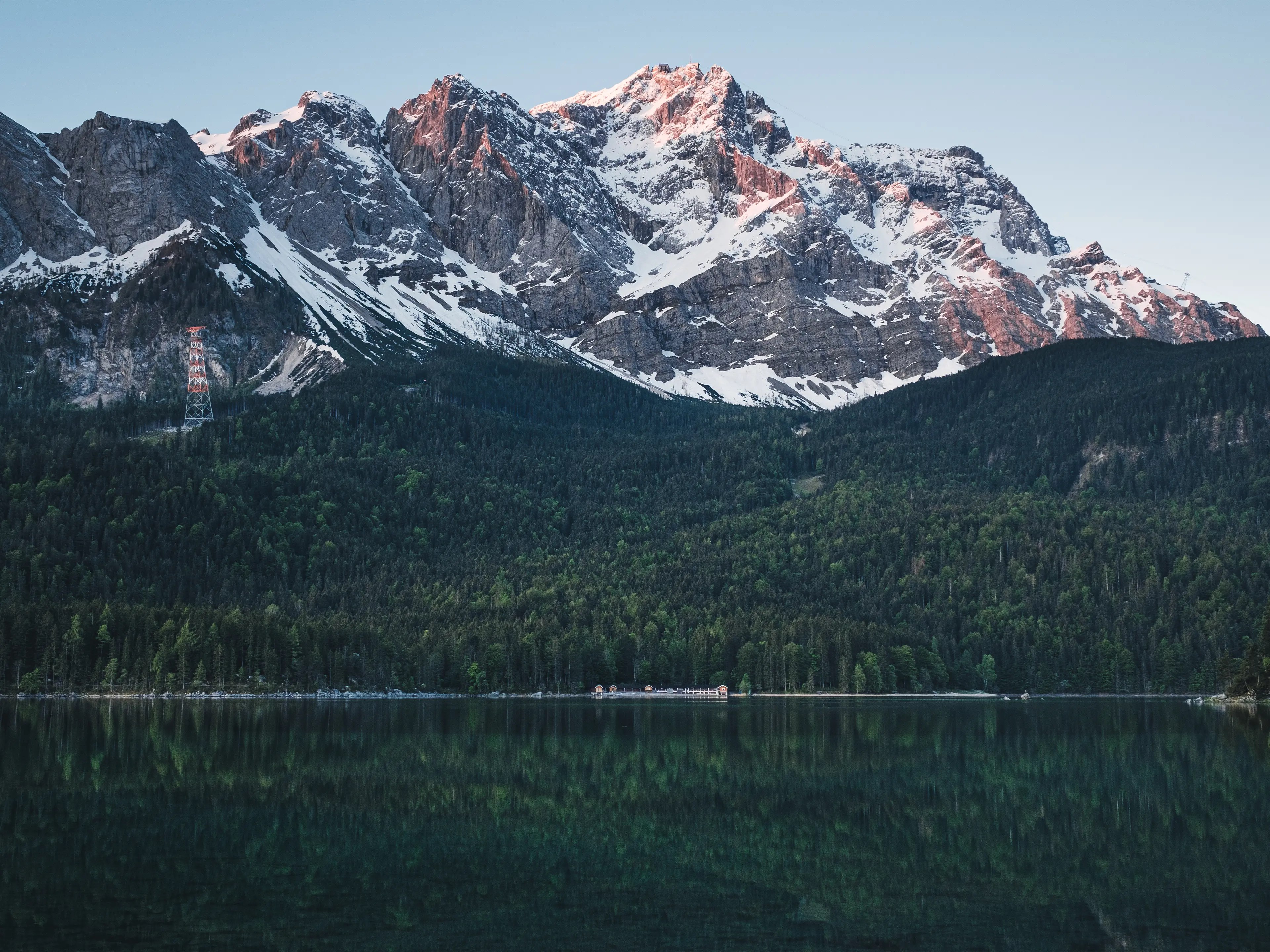 Die Zugspitze leuchtet in einem sanften Rot zum Sonnenaufgang und ist noch teilweise mit Schnee bedeckt.