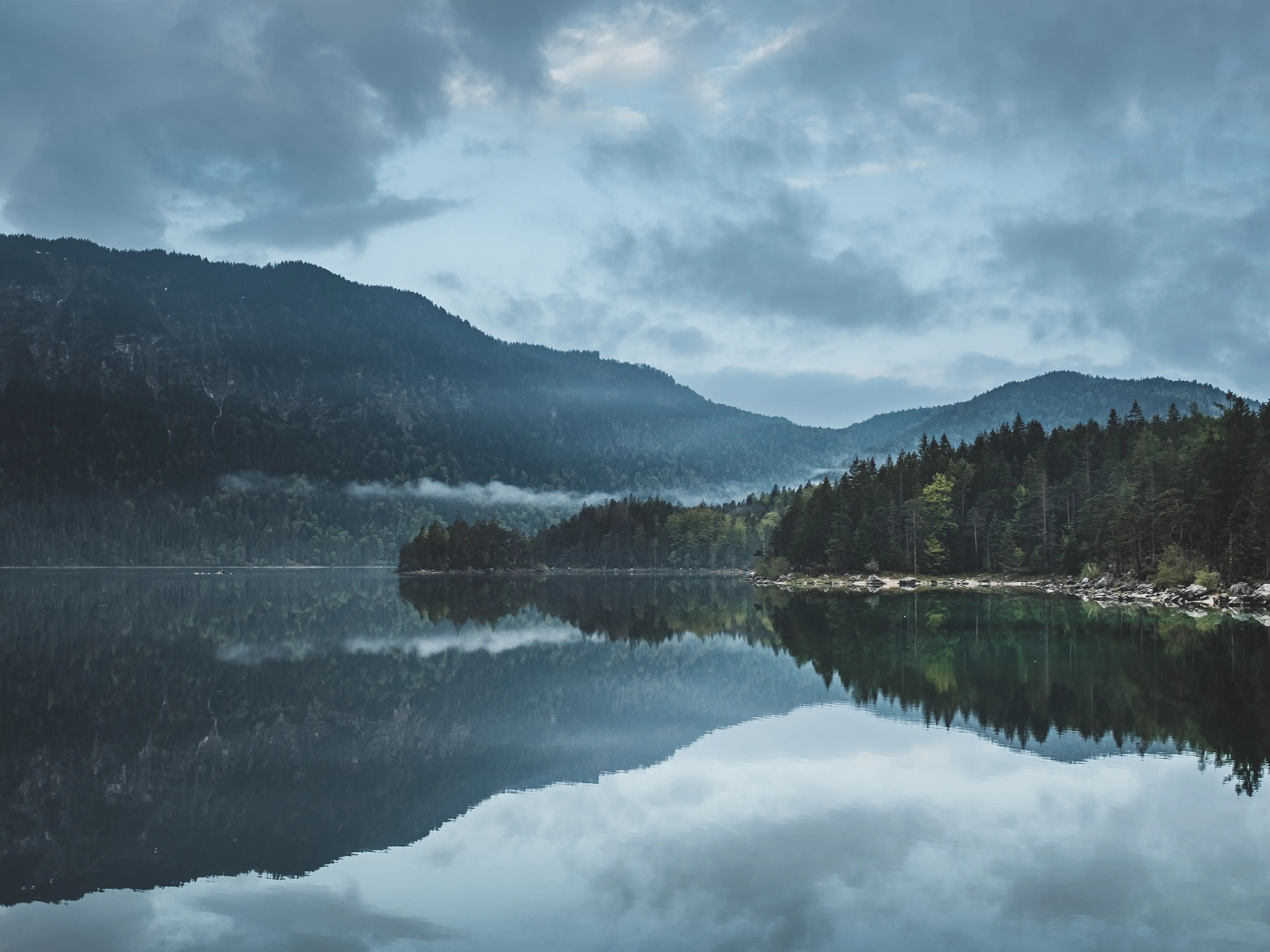 Wolken und Wälder spiegeln sich in der glatten Oberfläche des Eibsees.
