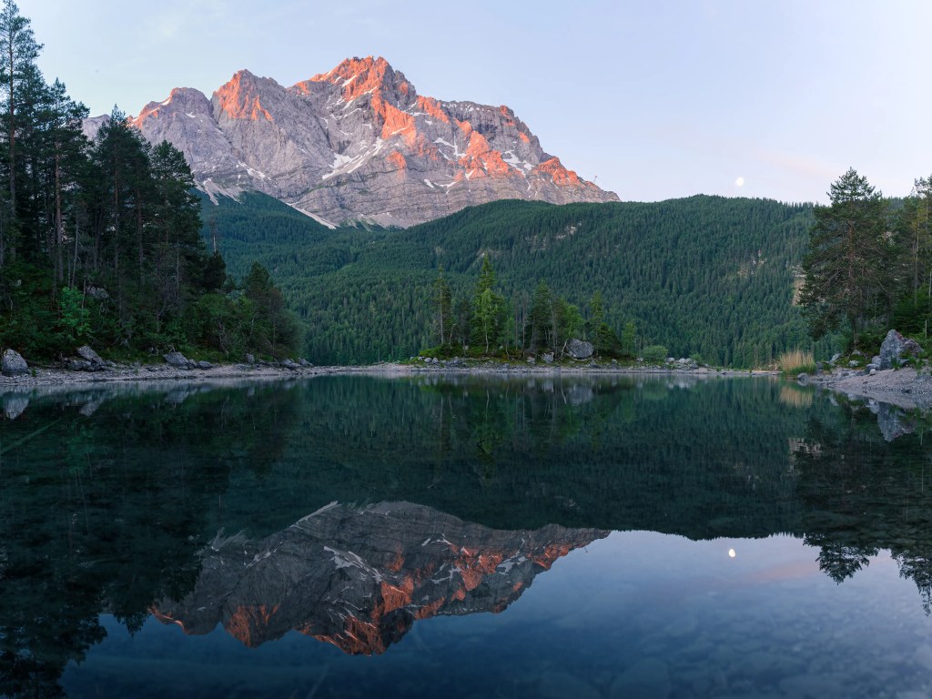 Die Zugspitze leuchtet im Licht der Vormittagssonne. Im Vordergrund ist eine kleine Insel mit Bäumen zu sehen.