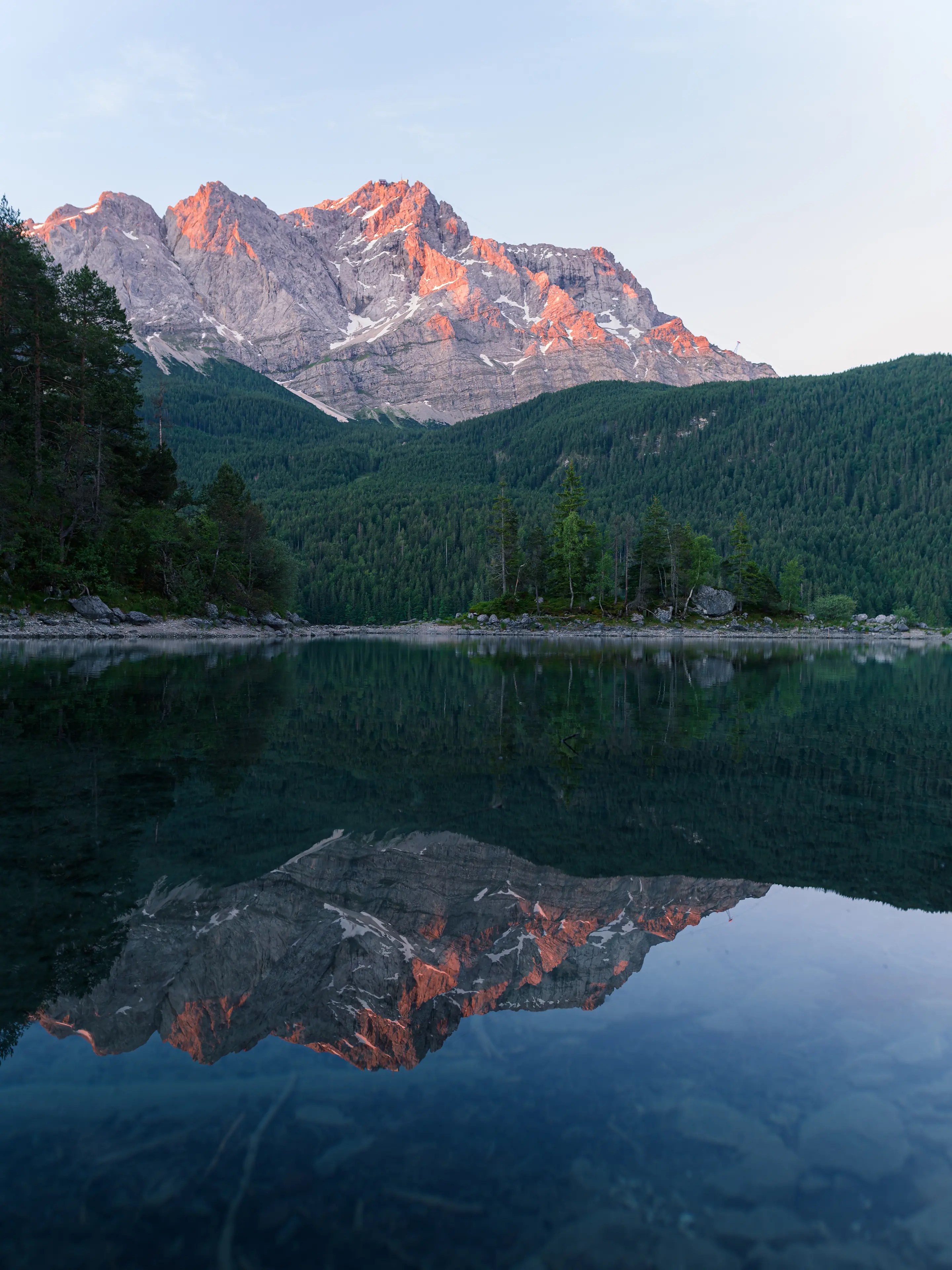 Die Zugspitze leuchtet im Licht der Vormittagssonne. Im Vordergrund ist eine kleine Insel mit Bäumen zu sehen.