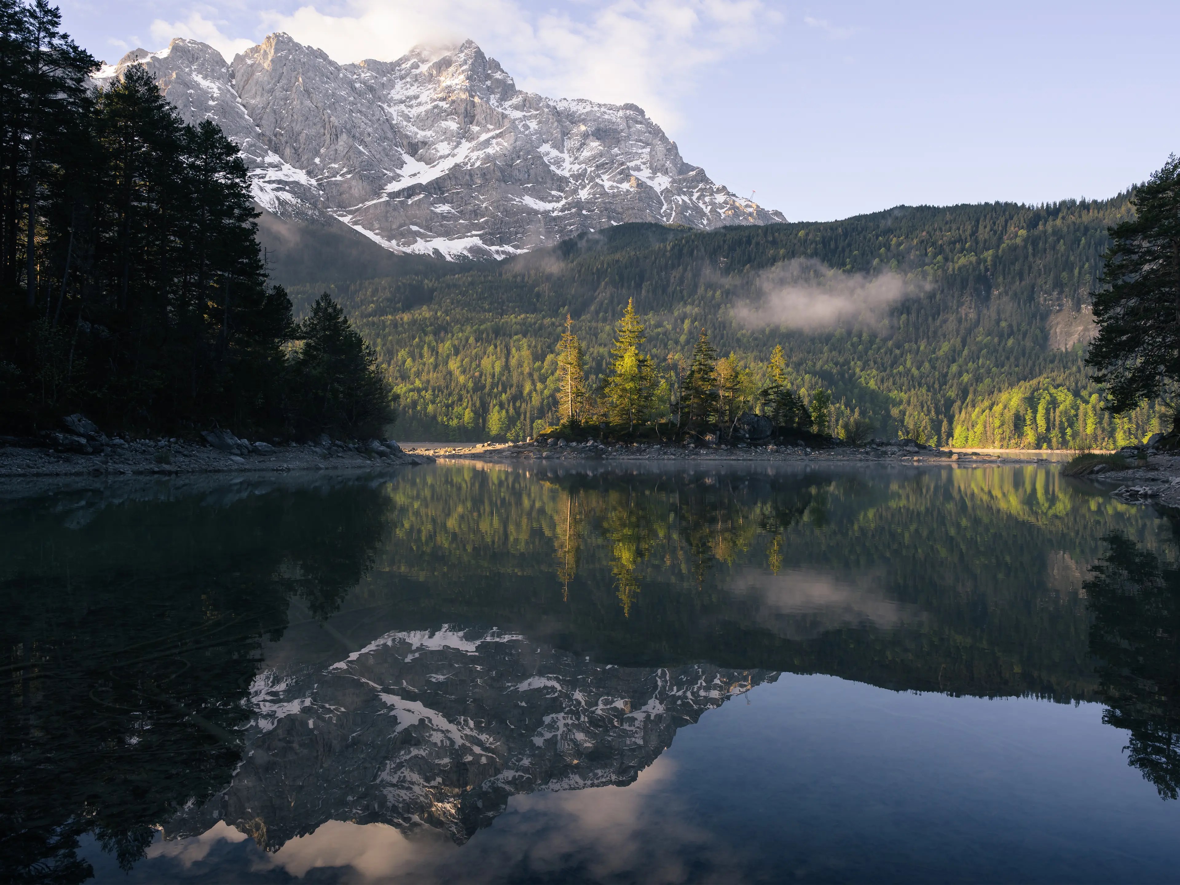 Die Zugspitze leuchtet im Licht der Vormittagssonne. Im Vordergrund ist eine kleine Insel mit Bäumen zu sehen.