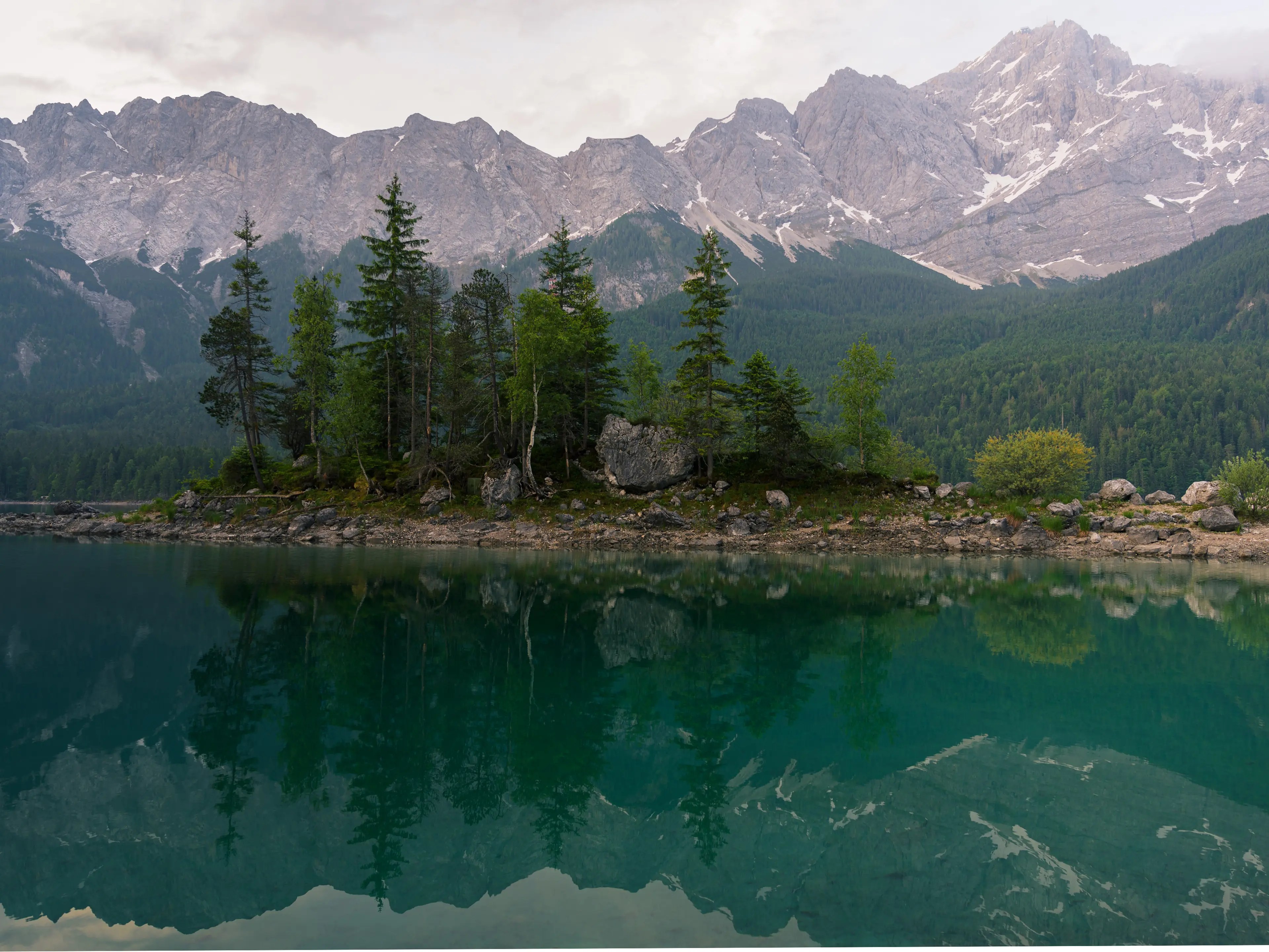 Die Zugspitze leuchtet im Licht der Vormittagssonne. Im Vordergrund ist eine kleine Insel mit Bäumen zu sehen.