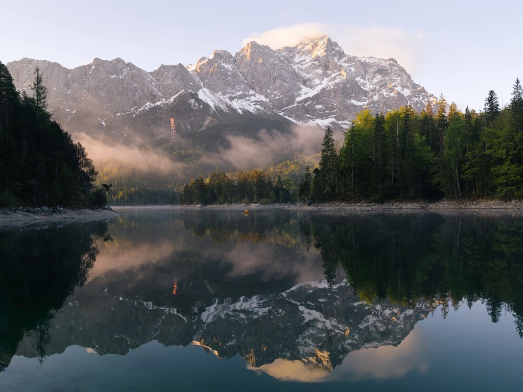 Ein Bild des Eibsees zum Sonnenaufgang. Die Zugspitze leuchtet im Morgenlicht und spiegelt sich im See.