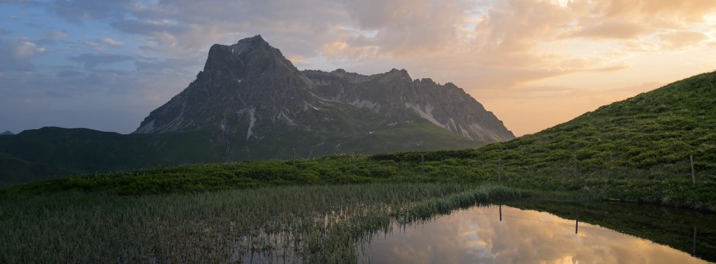 Eine Berglandschaft im Morgenlicht, im Vordergrund ist ein See