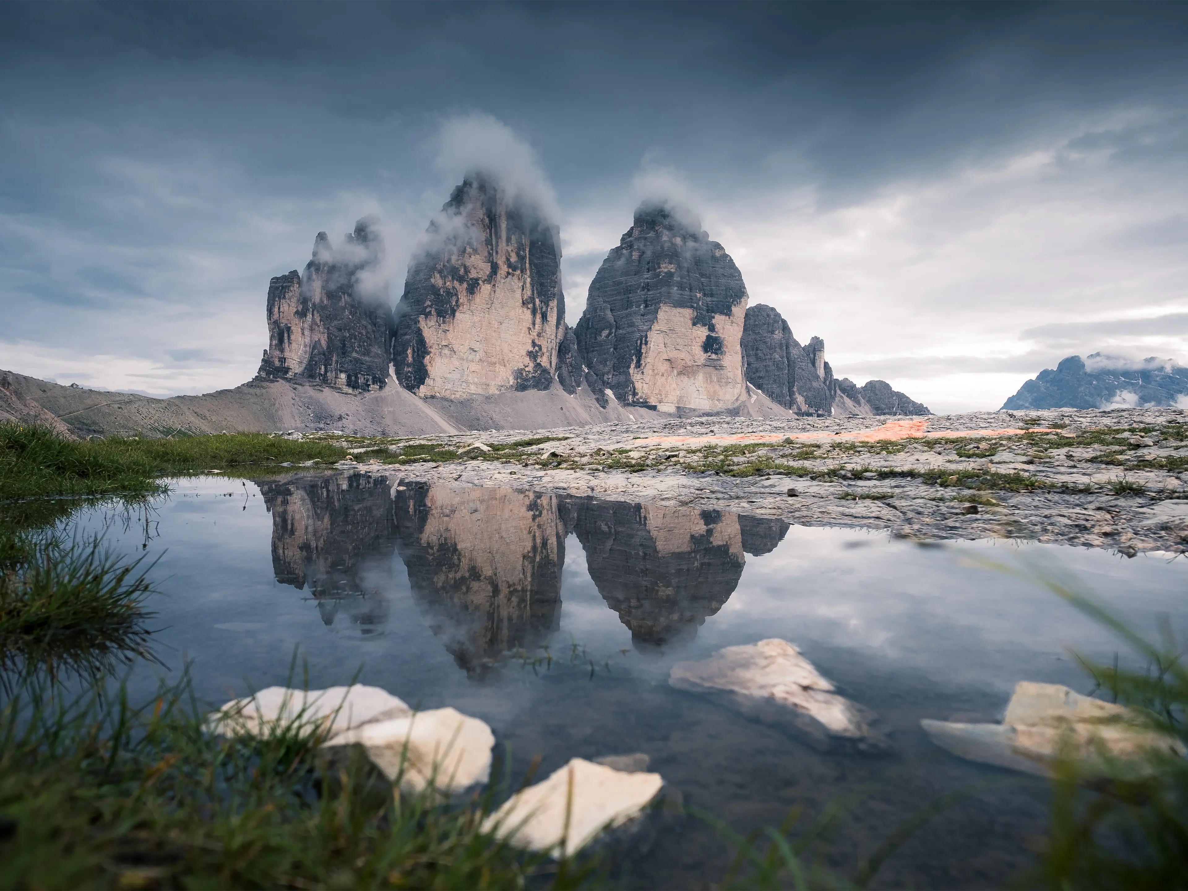 Die Drei Zinnen von Norden aus gesehen an bewölkten Sommertag mit einer kleinen Wasserlache 