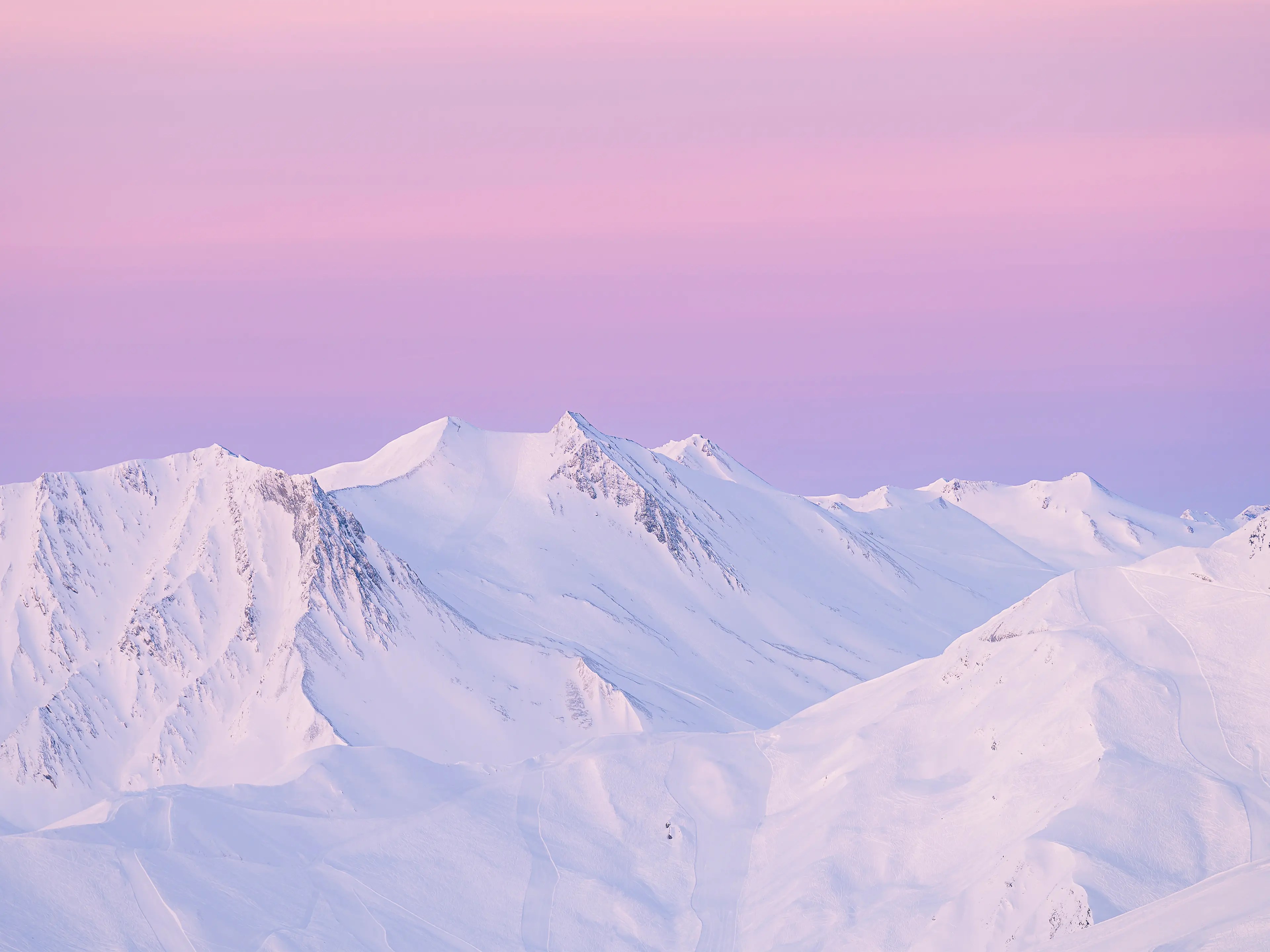 Berge mit verschneiten Gipfel ragen aus der Nebeldecke. Der Himmel ist in einem kräftigen orange gefärbt.