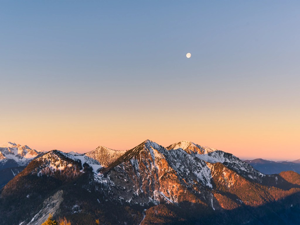 Der Herzogstand bedeckt mit einer dünnen Schneedecke, leuchtet orange und rot im Morgenlicht.
