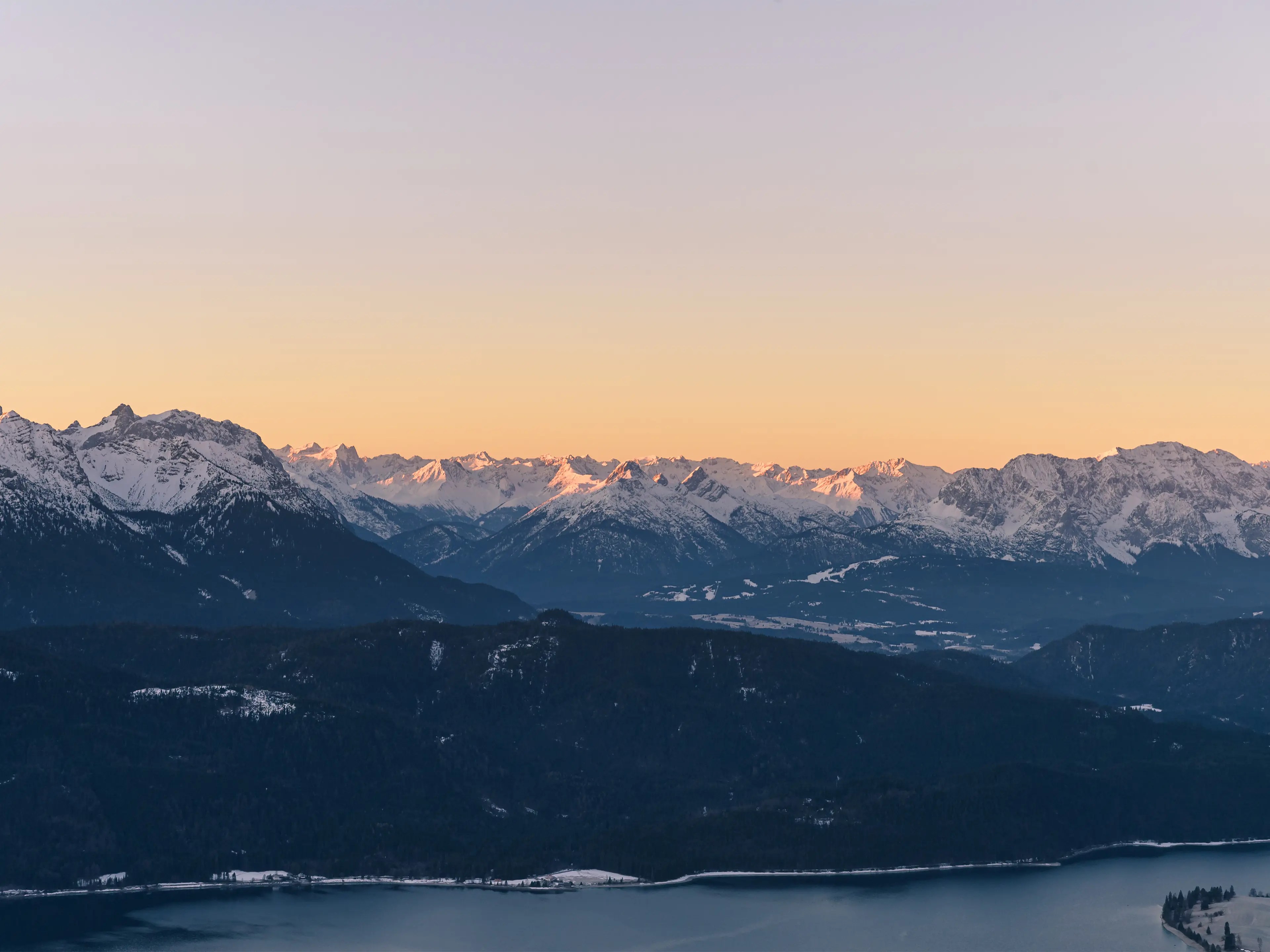 Blick zum Alpenhauptkamm vom Jochberg über den Walchensee. Die Gipfel sind mit Schnee bedeckt.