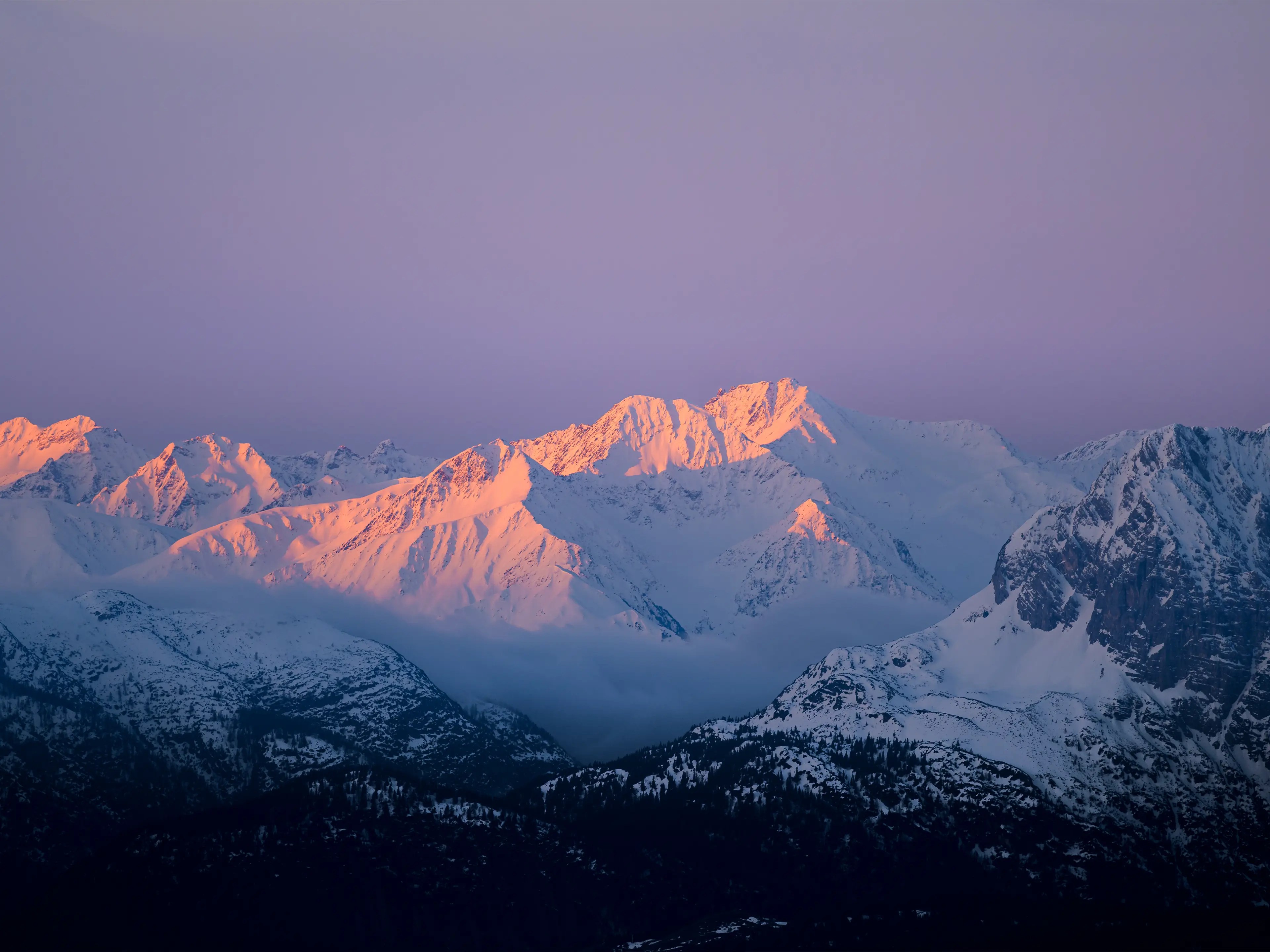 Im Morgenlicht rot und orange leuchtende Berge , die mit Schnee bedeckt sind.