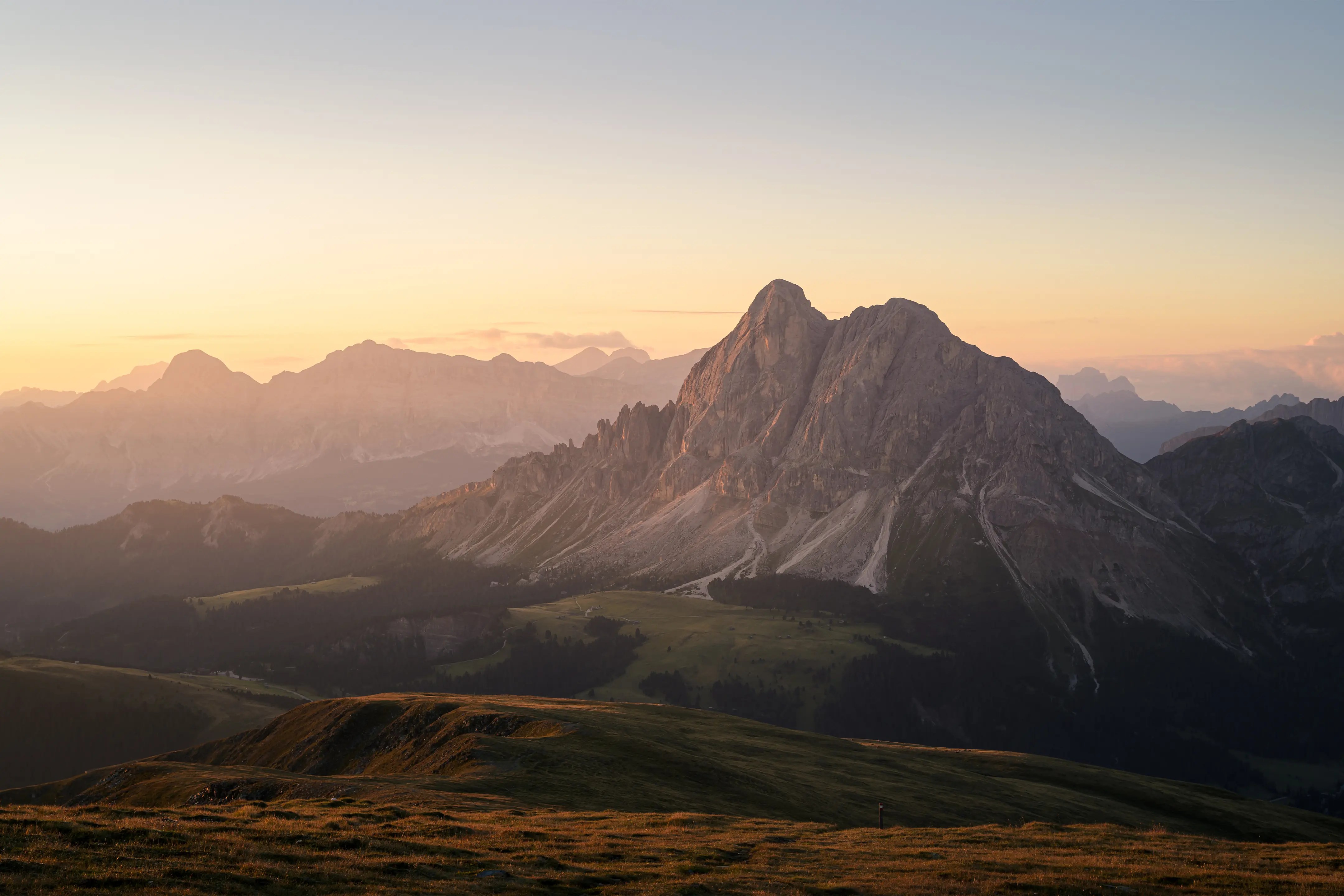 Blick auf felsige Berggipfel umgeben von mit Gras bedeckten Hügeln im warmen Morgenlicht.