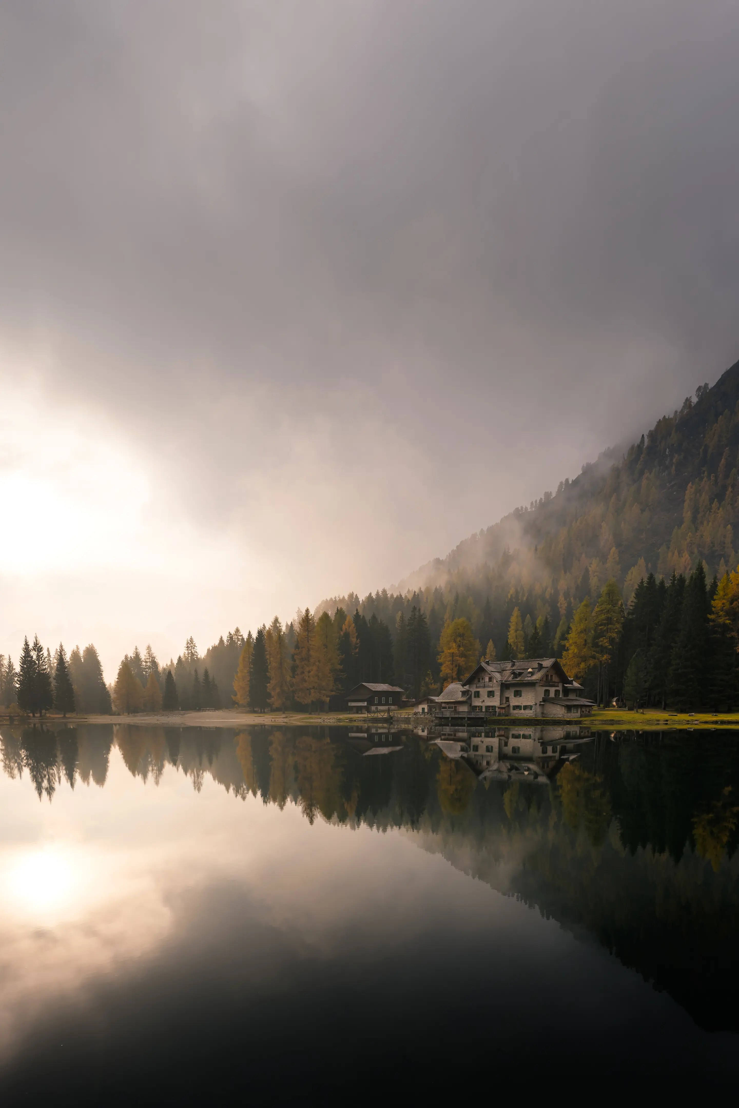 Eine Hütte an einem Bergsee, die sich in dessen Wasser spiegelt. Der Himmel ist nebelverhangen.