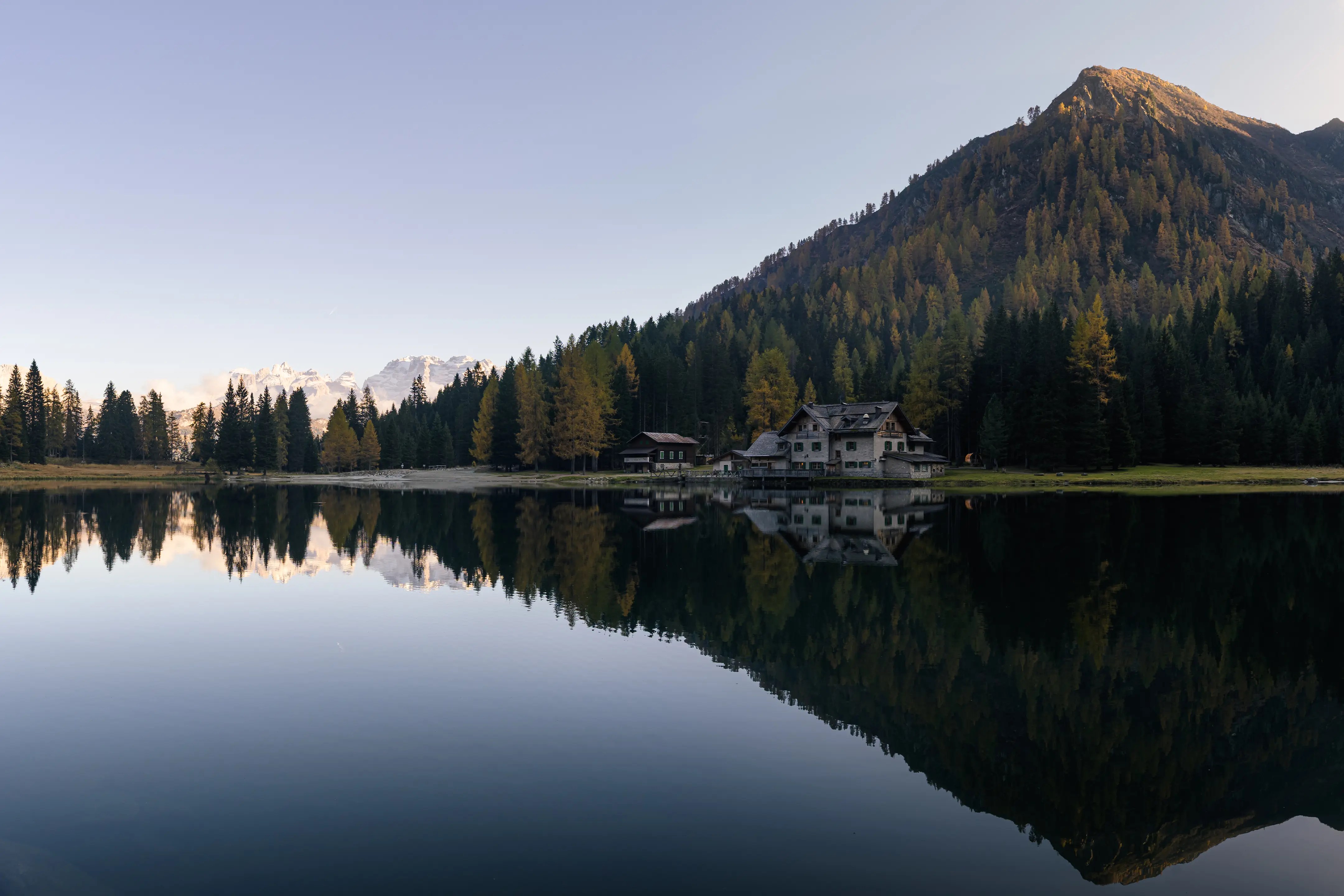 Eine Hütte an einem Bergsee, die sich in dessen Wasser spiegelt. Der Himmel ist klar.