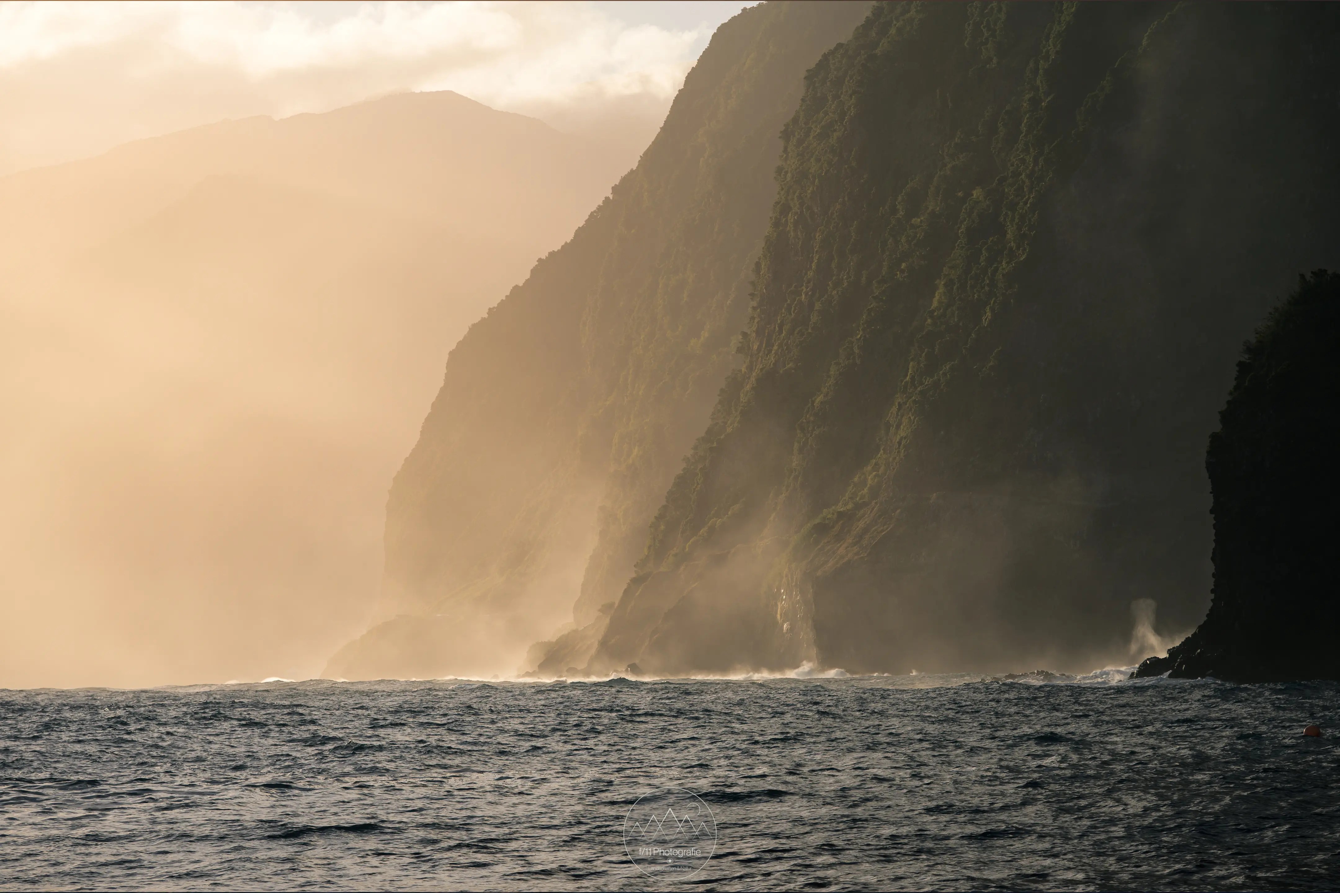 Die Steilklippen Madeira im goldenen Morgenlicht. Gischt steigt aus dem Meer auf.