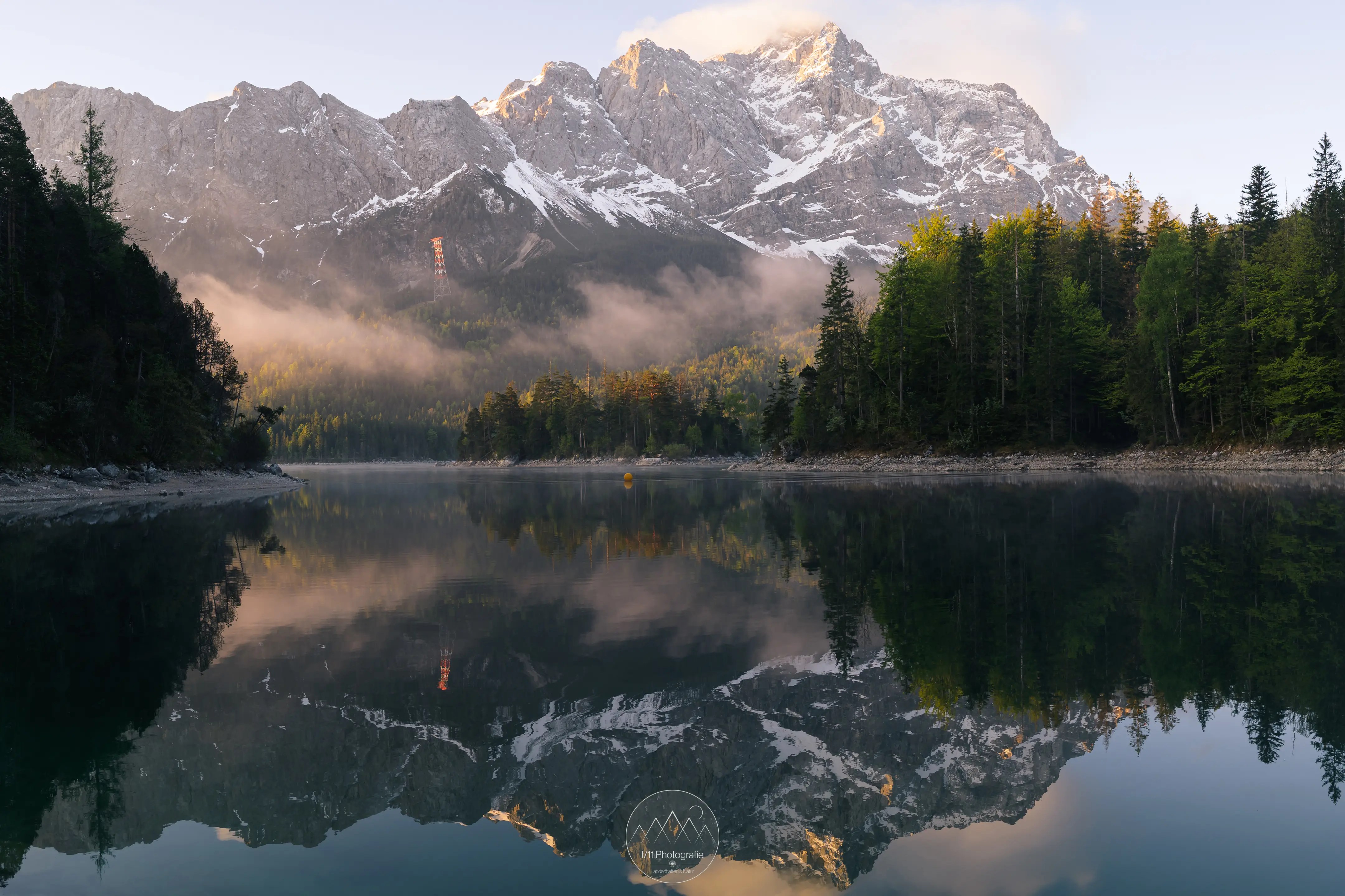 Nebel zieht über den See und der Gipfel der Zugspitze leuchtet im Morgenlicht, Bediungungen wie diese machen das Fotografieren am Eibsee immer wieder reizvoll.