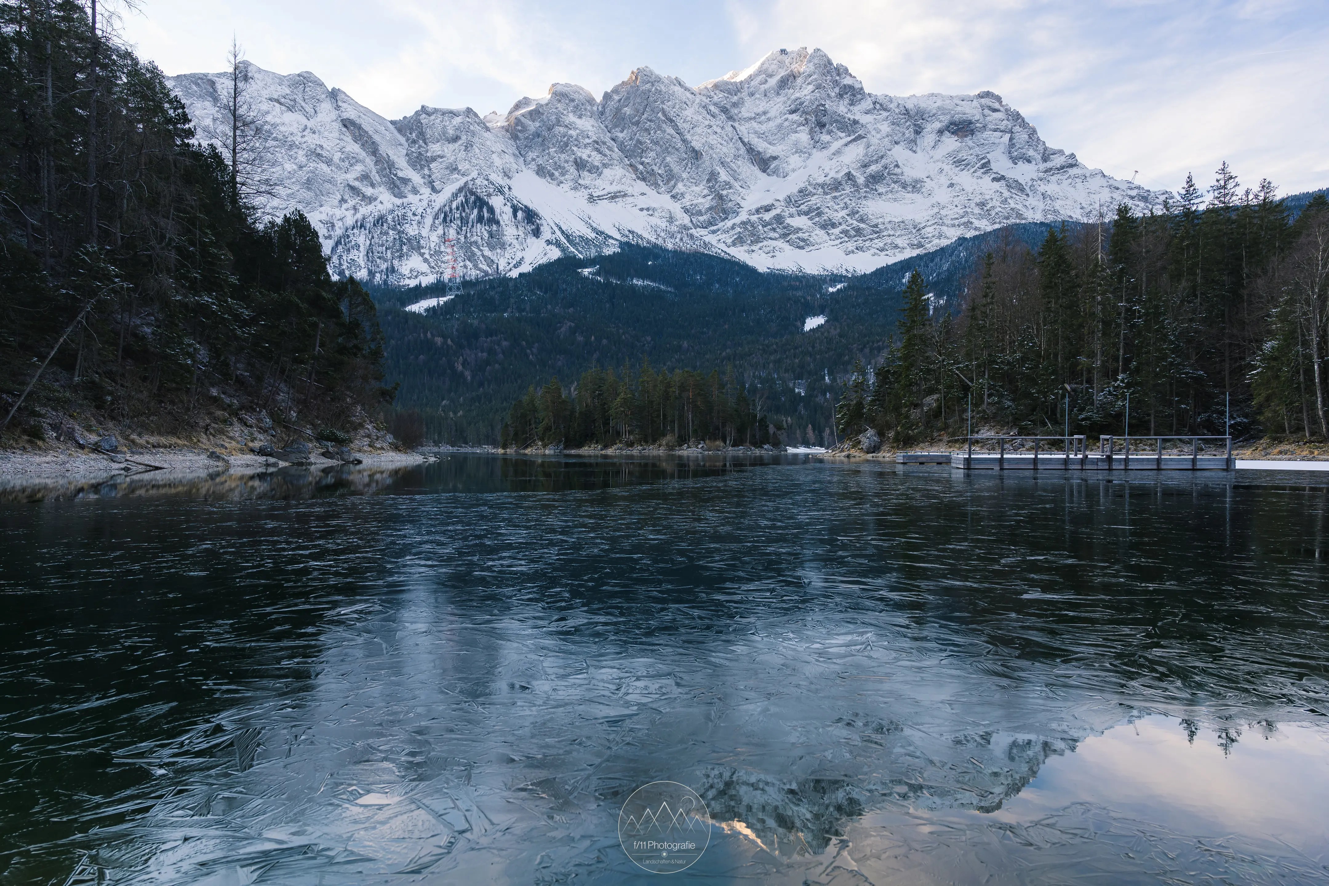 Im März ist der Eibsee meist noch teilweise zugefroren. Die schneebeckten Gipfel rund um die Zugspitze leuchten nur leicht in der Morgensonne.
