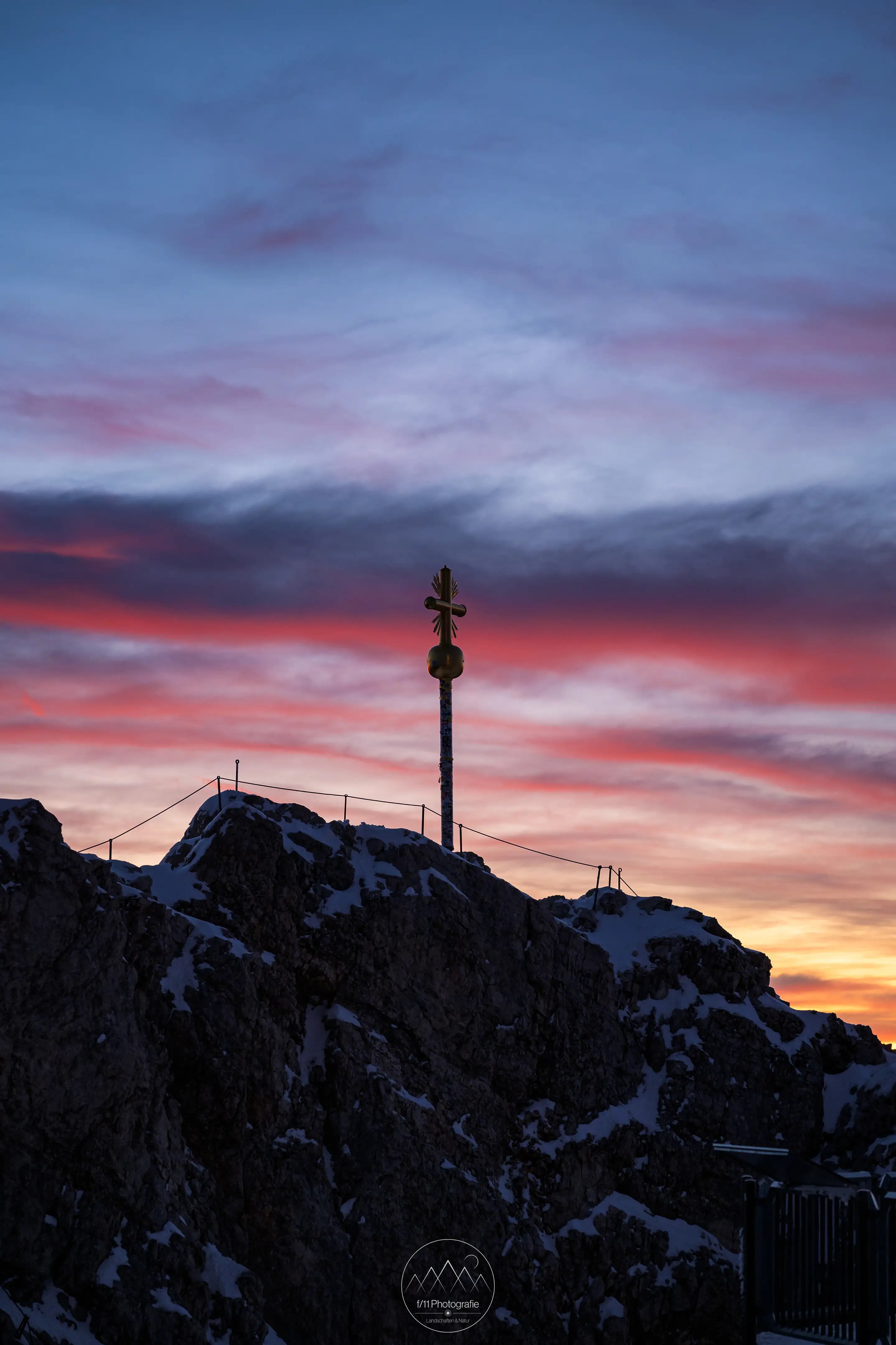 Das Gipfelkreuz der Zugspitze vor Sonnenaufang mit einem stimmungsvollen Himmel.