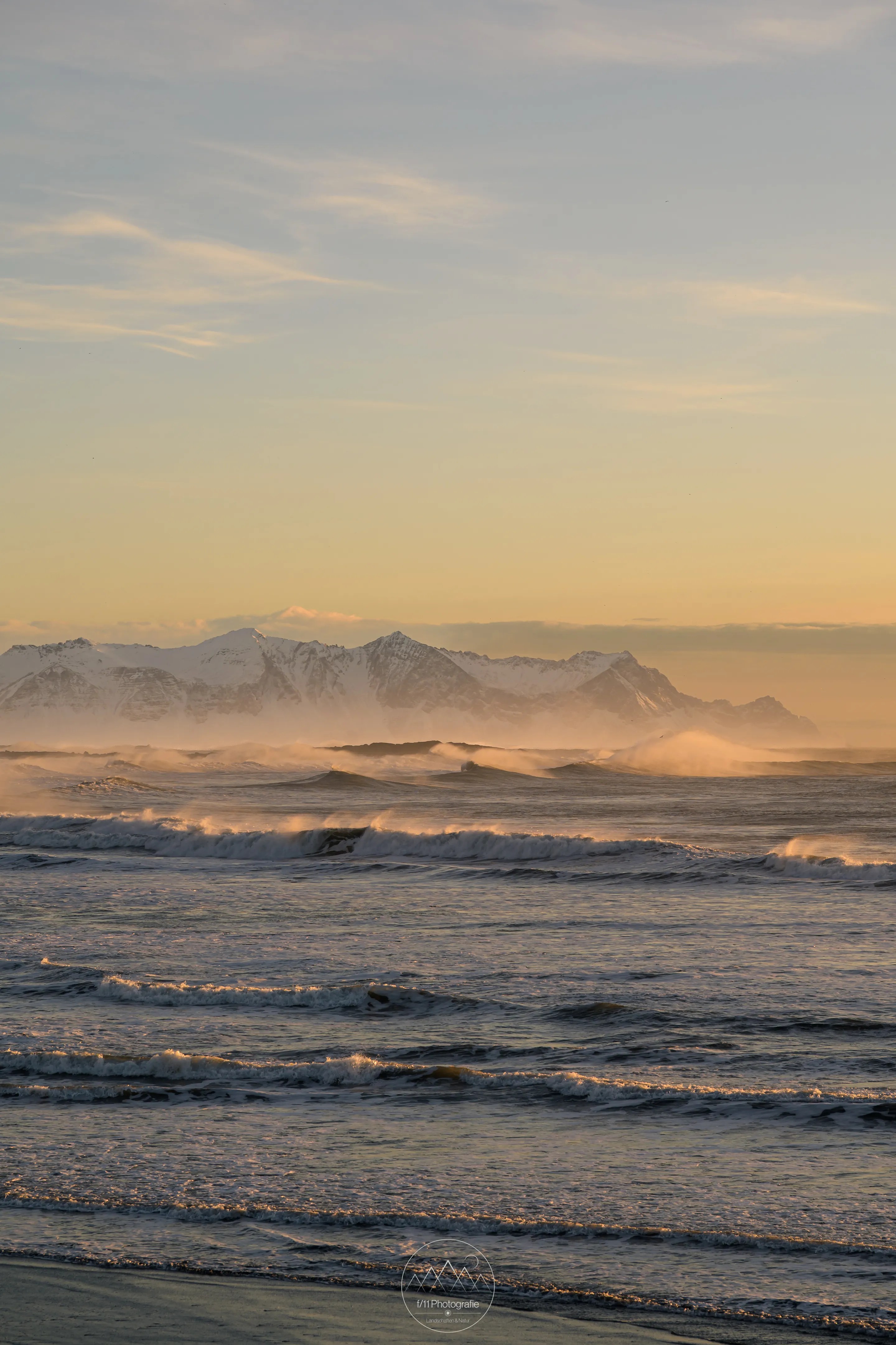 Ein rauer Wintermorgen am Strand von Stokksnes. Durch die Gischt der Wellen ist andere Seite der Küste erkennbar.